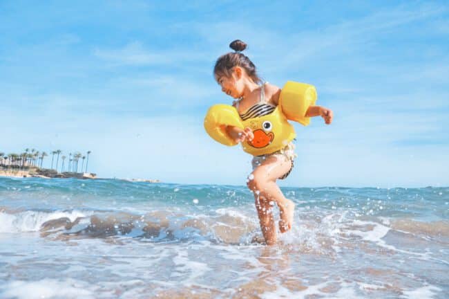 ילדה עם מצופים משחקת ליד ים בצהריים